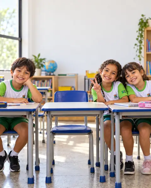 Três alunos sorrindo nas carteiras da sala